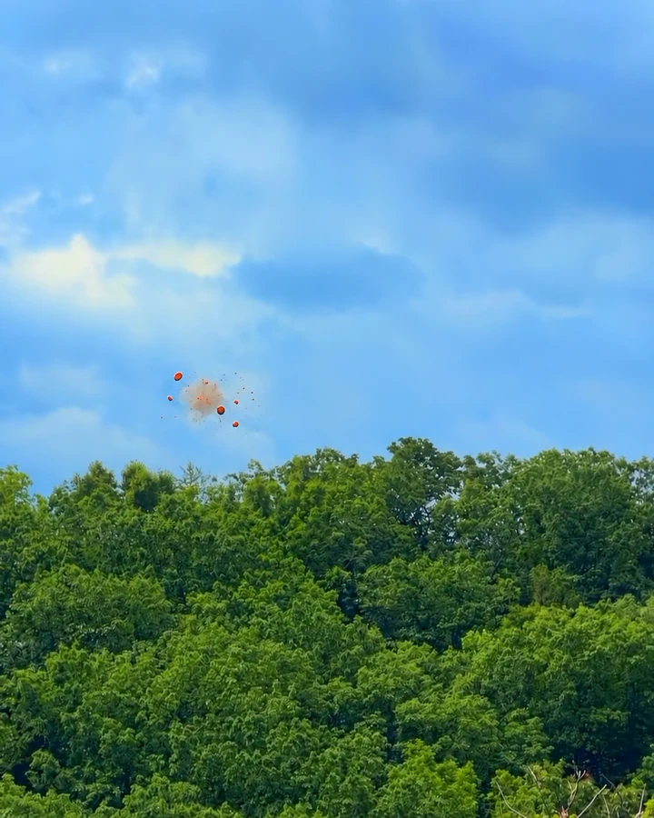An orange clay target breaking into fragments and dust against blue sky above the treetops