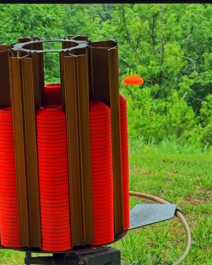 Loaded clay launcher releasing an orange disc against a wooded background